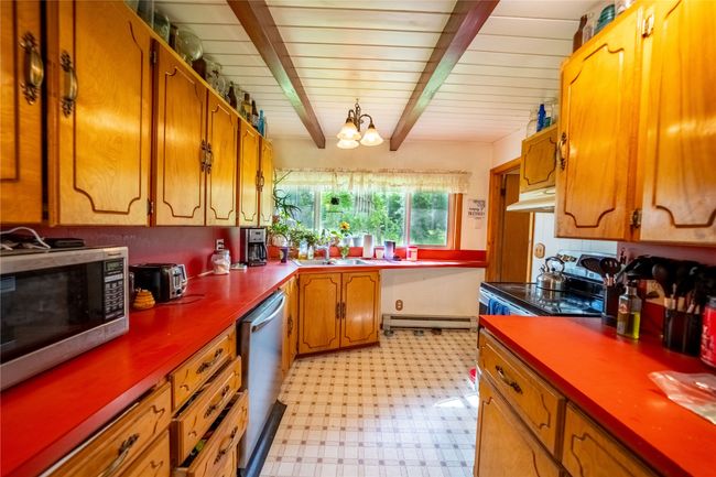 Kitchen featuring appliances with stainless steel finishes, baseboard heating, under cabinet range hood, light floors, and beam ceiling | Image 5
