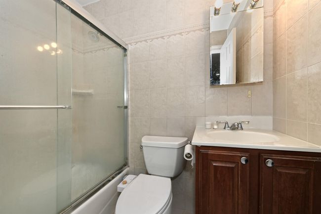 Bathroom with combined bath / shower with glass door, toilet, vanity, tasteful backsplash, and tile walls | Image 20
