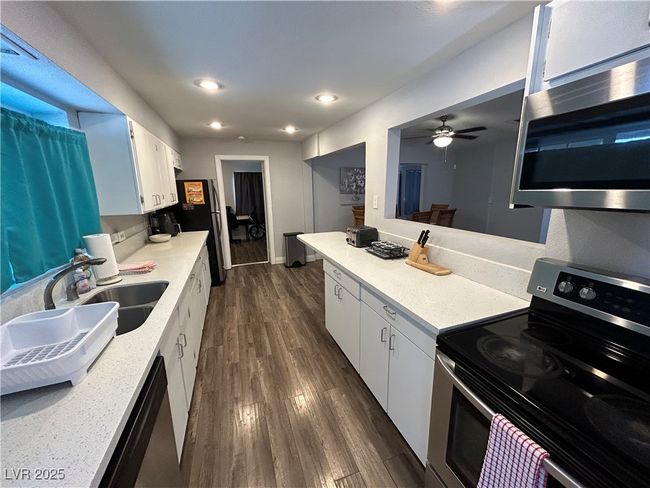 Kitchen with stainless steel appliances, ceiling fan, white cabinets, light countertops, and dark wood-style flooring | Image 4