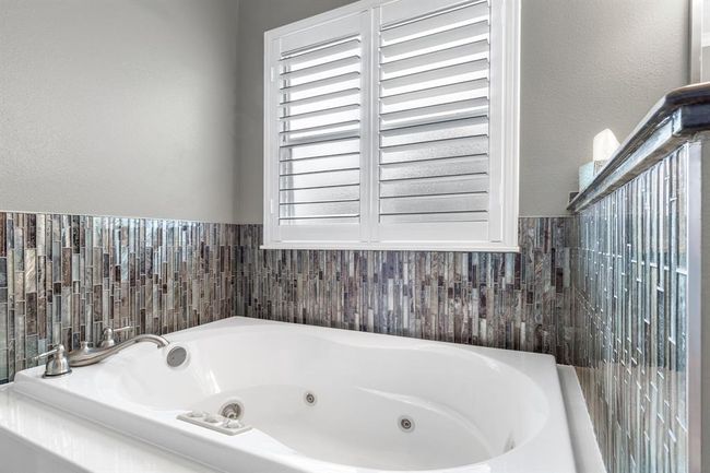 This bathroom features a sleek, modern bathtub with stylish mosaic tile accents and a window with plantation shutters, creating a bright and relaxing space. | Image 18