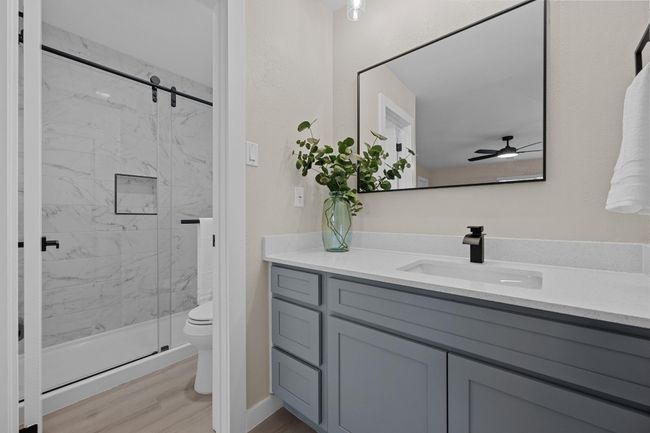 Bathroom featuring toilet, vanity, a ceiling fan, a marble finish shower, and wood finished floors | Image 13