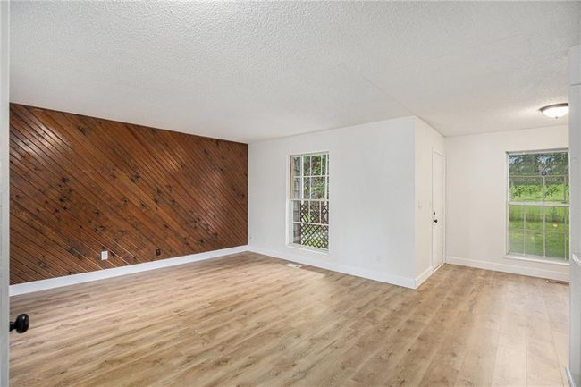 Spare room with baseboards, light wood-style flooring, wood walls, a textured ceiling, and an accent wall | Image 4