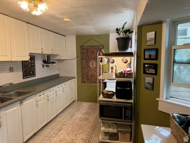 Kitchen with white cabinets, backsplash, light tile patterned floors, stainless steel microwave, and a sink | Image 23
