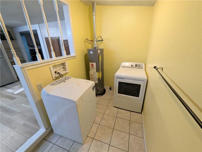 Laundry area featuring water heater, washer and dryer, light tile patterned floors, and a textured ceiling | Image 26
