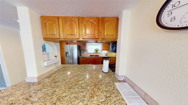 Kitchen featuring a textured wall, a textured ceiling, light stone countertops, appliances with stainless steel finishes, and brown cabinetry | Image 28