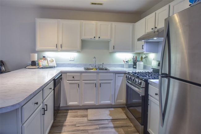 Kitchen with stainless steel appliances, under cabinet range hood, a sink, a peninsula, and white cabinetry | Image 6