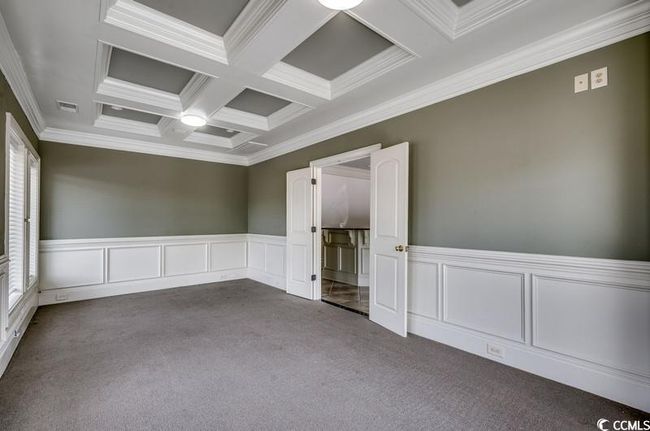 Empty room featuring dark carpet, coffered ceiling, crown molding, beamed ceiling, and a wainscoted wall | Image 13