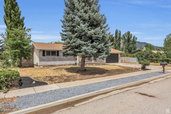 View of property hidden behind natural elements featuring brick siding, an attached garage, fence, and driveway | Image 6