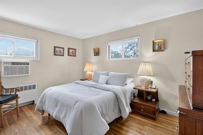 Bedroom with radiator heating unit, wood finished floors, and a wall unit AC | Image 9