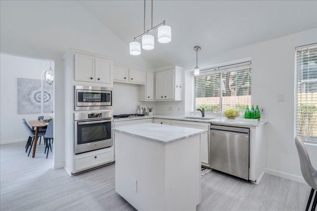 Kitchen with stainless steel appliances, a sink, light wood-type flooring, lofted ceiling, and a center island | Image 9