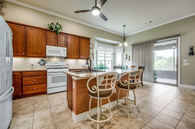 Kitchen with white appliances, backsplash, plenty of natural light, crown molding, and a center island with sink | Image 4