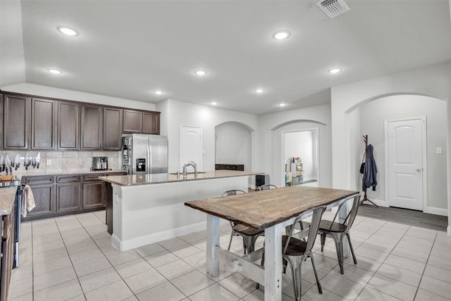 Kitchen featuring stainless steel refrigerator with ice dispenser, arched walkways, light tile patterned floors, dark brown cabinetry, and recessed lighting | Image 5