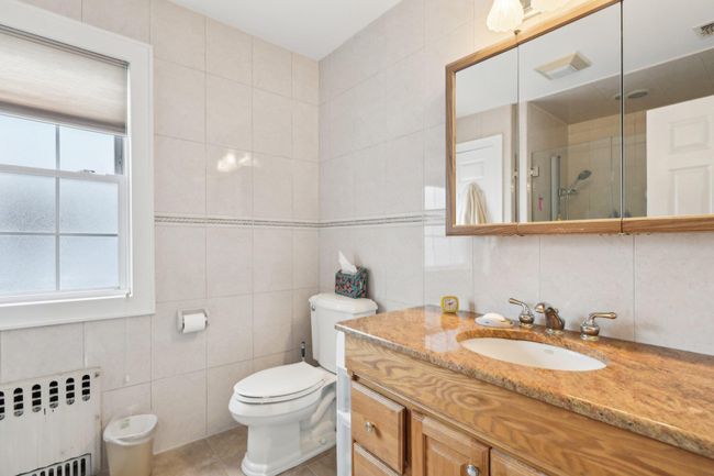 Bathroom featuring toilet, an enclosed shower, tile walls, vanity, and radiator | Image 21