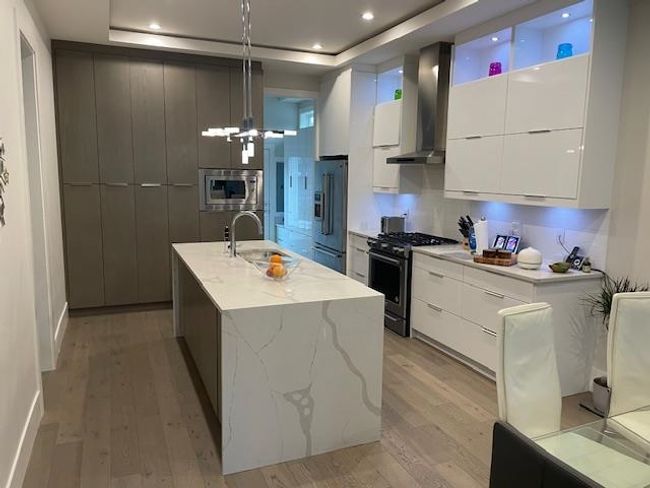 Kitchen featuring a raised ceiling, wall chimney range hood, stainless steel appliances, and modern cabinets | Image 7