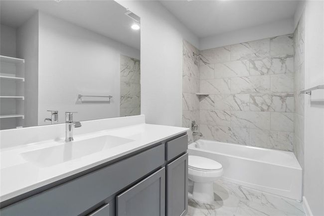 Secondary bath features tile flooring, bath/shower combo with tile surround, stained wood cabinets, beautiful light countertops, mirror, sleek fixtures and modern finishes! | Image 12