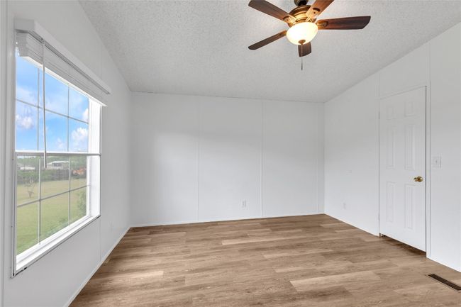 Empty room with a textured ceiling, light wood-type flooring, a ceiling fan, and lofted ceiling | Image 27