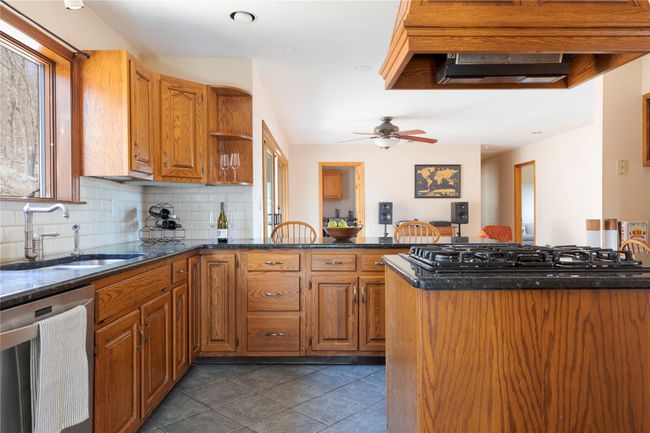 Kitchen with a peninsula, gas cooktop, dark stone countertops, a sink, and stainless steel dishwasher | Image 10