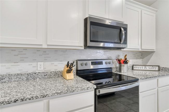 Kitchen with tile patterned flooring, backsplash, stainless steel appliances, light stone countertops, and white cabinets | Image 16