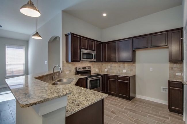 Kitchen with appliances with stainless steel finishes, a sink, a peninsula, light stone countertops, and arched walkways | Image 7