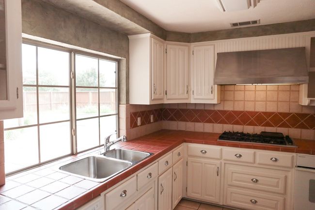 Kitchen with under cabinet range hood, black gas stovetop, tile counters, and oven | Image 29