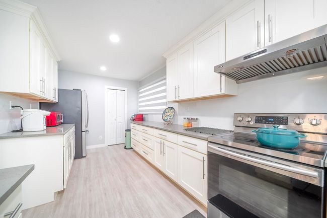 Kitchen with light wood-style flooring, white cabinets, exhaust hood, and stainless steel electric range | Image 23