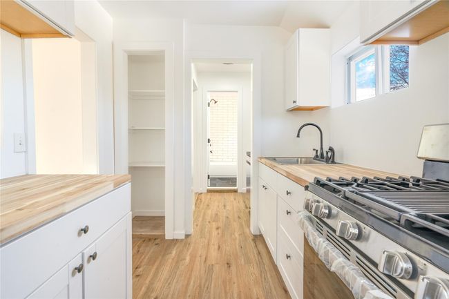 Kitchen with light wood-type flooring, a sink, stainless steel range with gas cooktop, white cabinets, and butcher block counters | Image 9