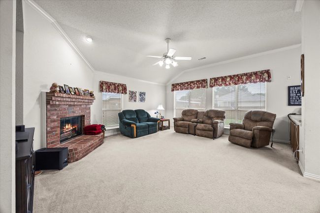 Living area featuring lofted ceiling, crown molding, carpet flooring, a ceiling fan, and a fireplace | Image 14