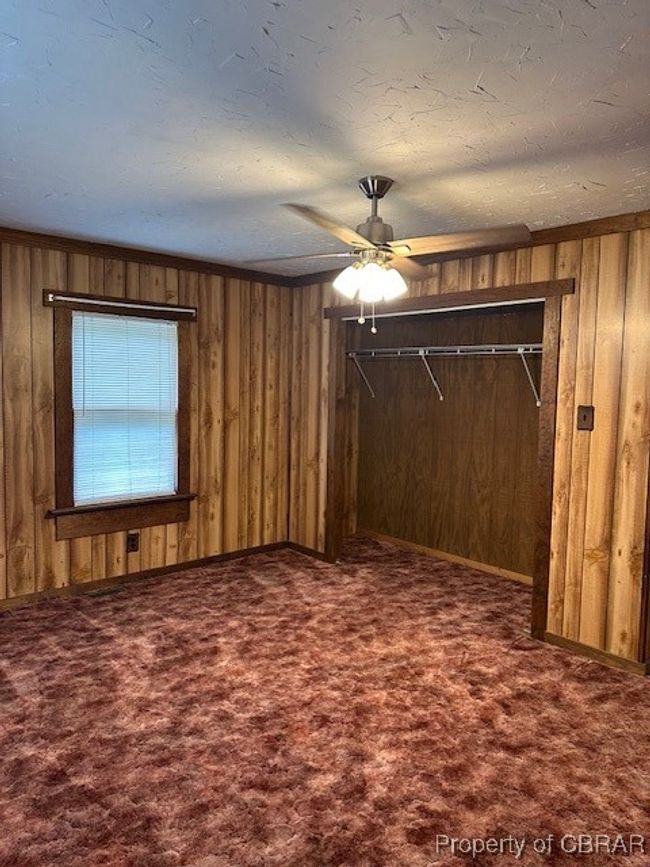 Unfurnished bedroom featuring carpet flooring, wood walls, a closet, and ceiling fan | Image 19
