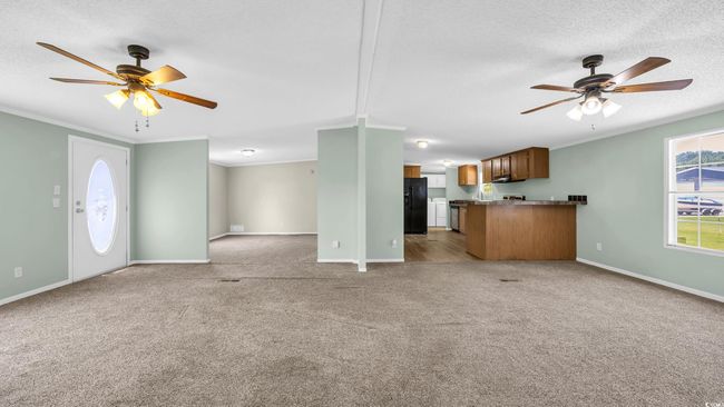 Unfurnished living room featuring ceiling fan, light colored carpet, a textured ceiling, and ornamental molding | Image 6