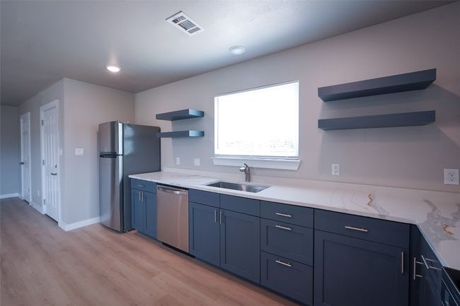 Kitchen featuring open shelves, appliances with stainless steel finishes, light wood-style floors, blue cabinets, and light stone countertops | Image 12