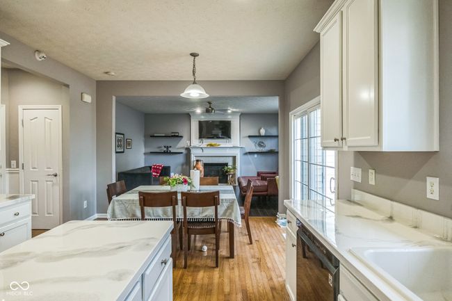 kitchen with dishwasher, a fireplace, light wood-style flooring, white cabinetry, and hanging light fixtures | Image 12