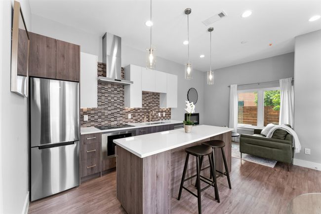 Kitchen with wall chimney range hood, visible vents, modern cabinets, a sink, and freestanding refrigerator | Image 7