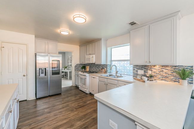 Kitchen with white appliances, dark wood-type flooring, decorative backsplash, light countertops, and a peninsula | Image 5