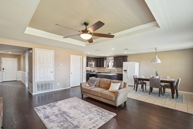 Living room featuring a ceiling fan, a tray ceiling, dark wood-type flooring, and visible vents | Image 9
