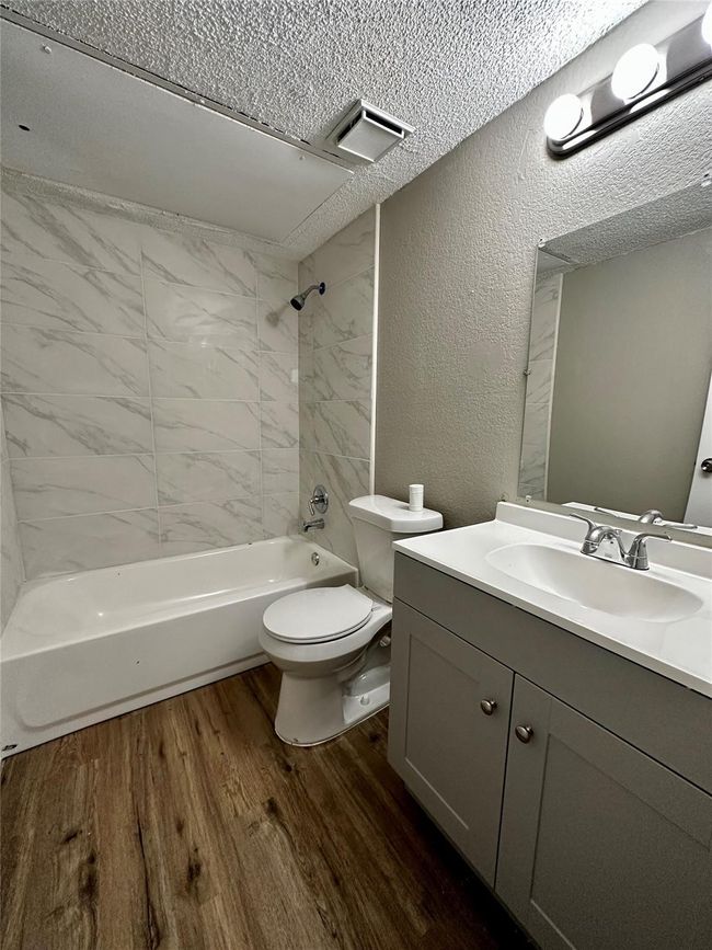 Full bathroom featuring a textured wall, wood finished floors, vanity, shower / bath combination, and toilet | Image 4