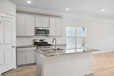 Kitchen featuring appliances with stainless steel finishes, light stone countertops, light wood-type flooring, and an island with sink | Image 3