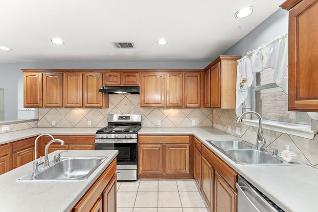 Kitchen with light countertops, a sink, under cabinet range hood, and stainless steel appliances | Image 15