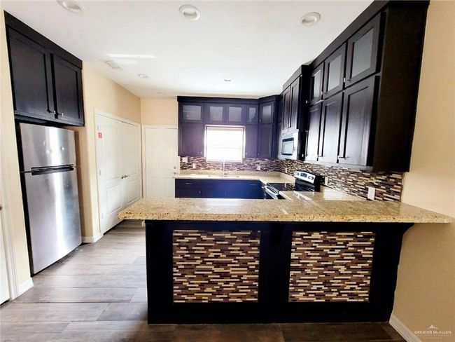Kitchen with stainless steel appliances, backsplash, a peninsula, glass insert cabinets, and light stone countertops | Image 4