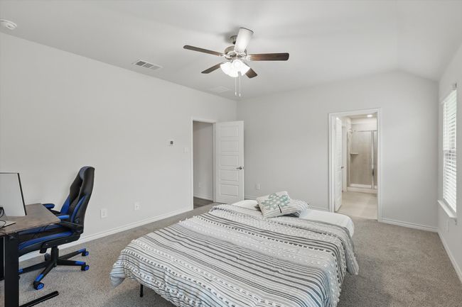 Carpeted bedroom with a desk, multiple windows, ceiling fan, ensuite bath, and lofted ceiling | Image 21