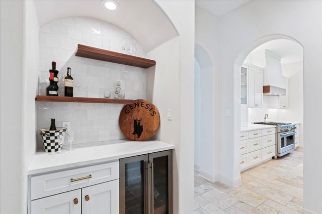 Indoor dry bar featuring range with two ovens, beverage cooler, decorative backsplash, custom exhaust hood, and stone tile flooring | Image 12
