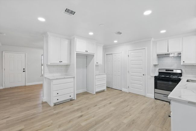 Kitchen featuring stainless steel gas stove, under cabinet range hood, crown molding, decorative backsplash, and light stone countertops | Image 7