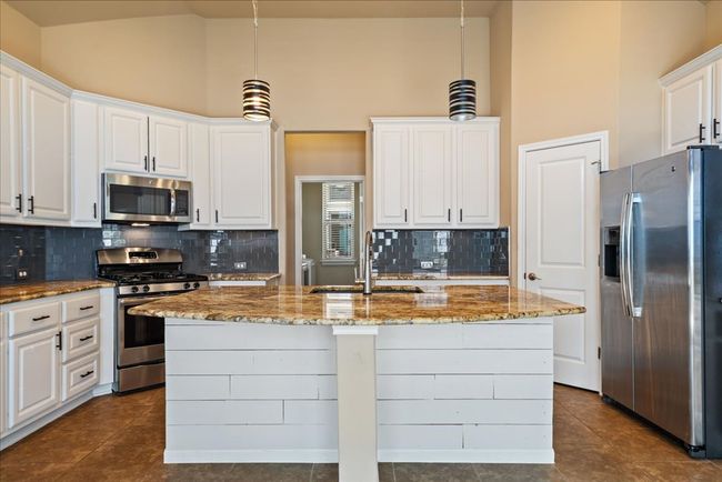 The kitchen has tile floor, stainless steel appliances, a decorative backsplash, a center island, and stylish white cabinets featuring pull out drawers. | Image 14