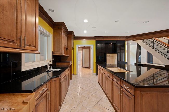 Kitchen featuring light tile patterned floors, crown molding, recessed lighting, brown cabinetry, and a large island with sink | Image 16
