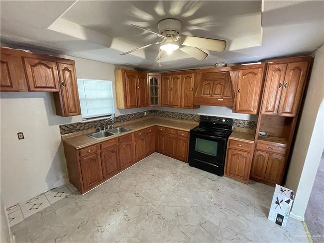 Kitchen with black electric range oven, a sink, and brown cabinets | Image 11