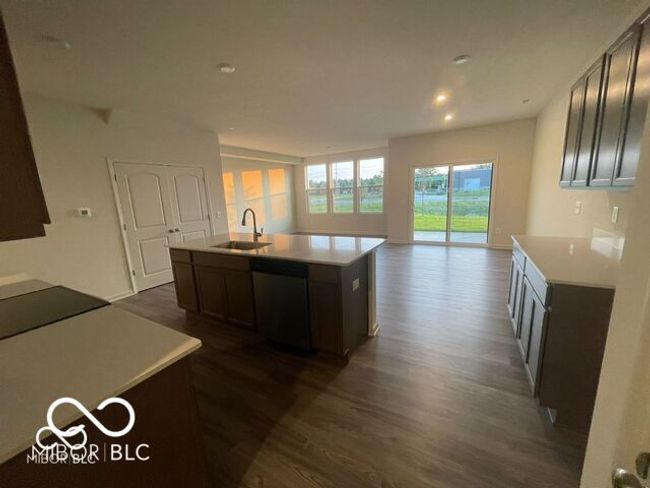 kitchen featuring stainless steel dishwasher, dark wood finished floors, light countertops, a sink, and a center island with sink | Image 6
