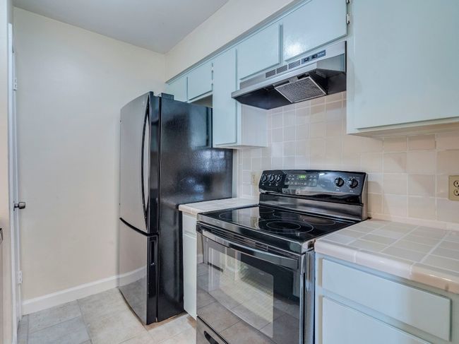 Kitchen featuring black appliances, tile countertops, under cabinet range hood, and backsplash | Image 7
