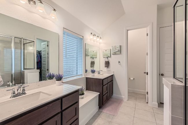 Bathroom with two vanities, a shower stall, lofted ceiling, tile patterned floors, and a walk in closet | Image 17