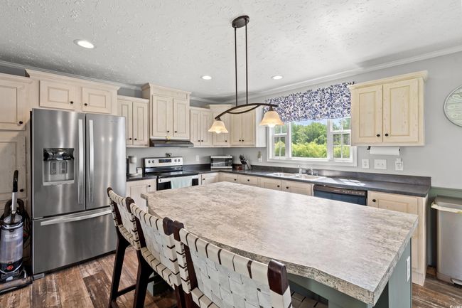 Kitchen featuring stainless steel appliances, under cabinet range hood, ornamental molding, a kitchen bar, and dark wood finished floors | Image 6