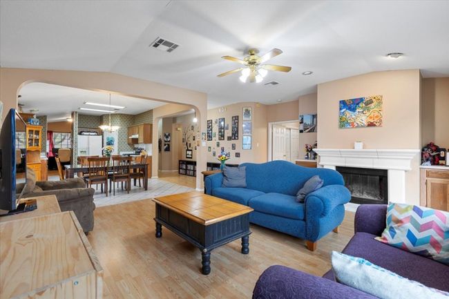 Living area featuring arched walkways, ceiling fan, a fireplace, light wood-style flooring, and lofted ceiling | Image 17