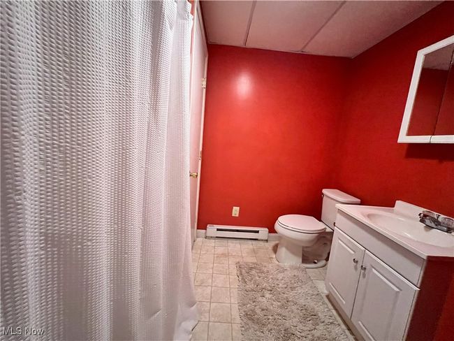 Bathroom with tile patterned floors, toilet, baseboard heating, curtained shower, and vanity | Image 28